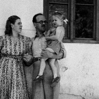 Man holding a baby, woman standing nearby outdoors.