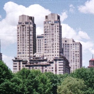 People relax in a park with city buildings in background.