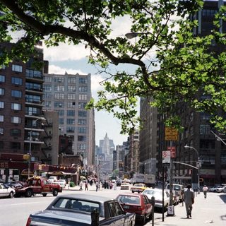 Street scene with cars, buildings, and people in a city.