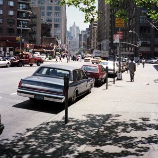 Street scene with cars, buildings, and people in a city.