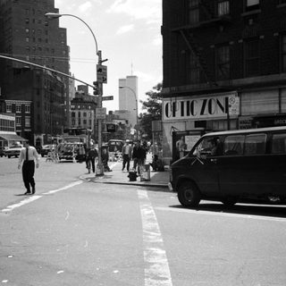 Street scene with people, vehicles, and storefront in a city.