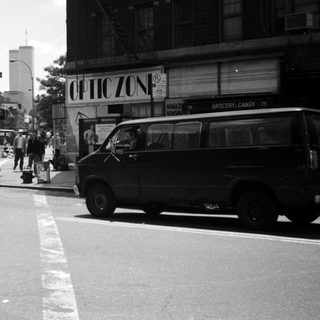 Street scene with people, vehicles, and storefront in a city.