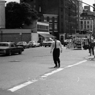 Street scene with people, vehicles, and storefront in a city.