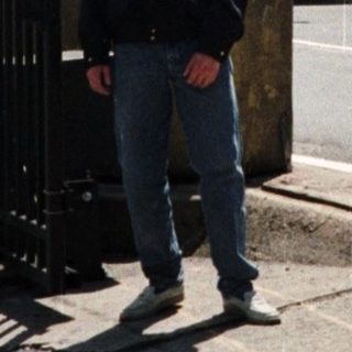 Man stands near Welcome to Manhattan sign, towers visible.