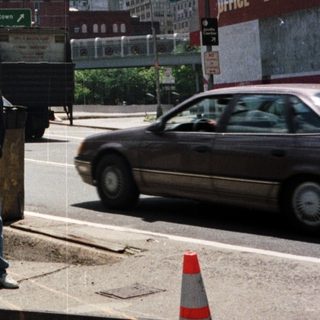 Man stands near Welcome to Manhattan sign, towers visible.