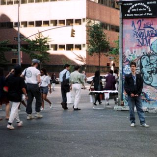 People stand near a graffiti-covered wall on a city street.