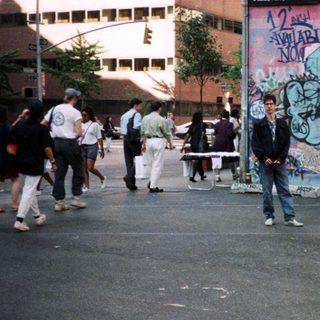 People stand near a graffiti-covered wall on a city street.