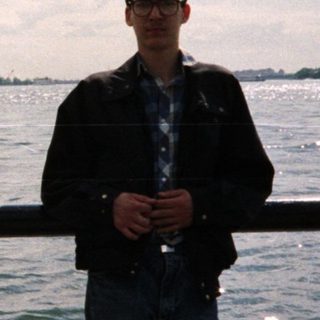 Man stands near water with Statue of Liberty in background.