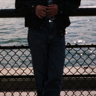 Man stands near water with Statue of Liberty in background.