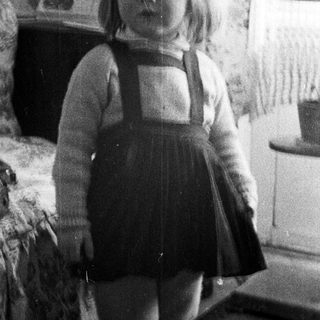 Here's a brief summary of the image: Black and white photo of a young girl in a dress.