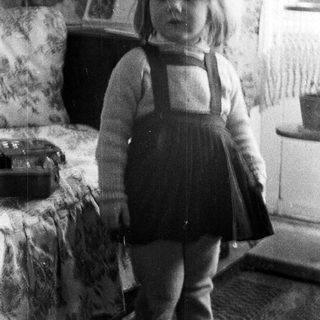 Here's a brief summary of the image: Black and white photo of a young girl in a dress.
