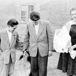 Three people and a dog stand outside a building.