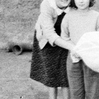 Two girls stand outside, one carrying a bag.