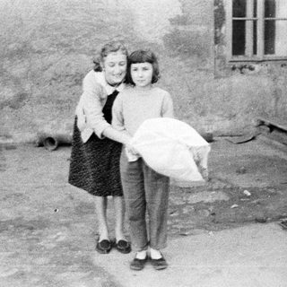 Two girls stand outside, one carrying a bag.