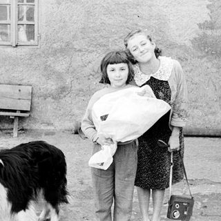 Two girls holding a baby outdoors with a dog.