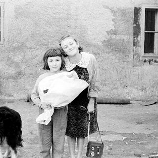 Two girls holding a baby outdoors with a dog.