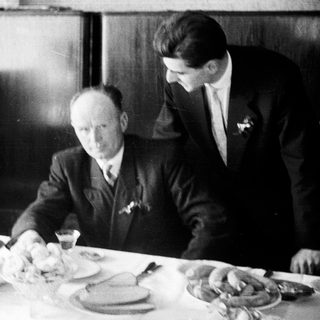 Here's a brief summary of the image: Men seated at a table, with a person in the background.