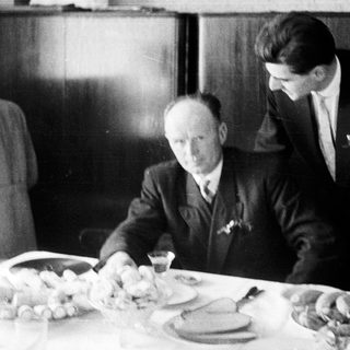 Here's a brief summary of the image: Men seated at a table, with a person in the background.
