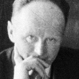 Man at table, boy stands nearby reading.