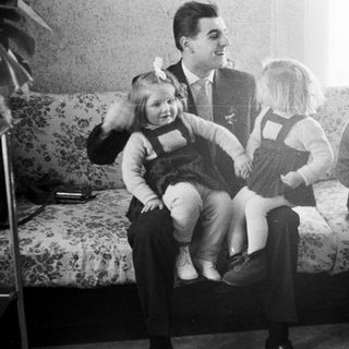Man sits with three young girls on a floral sofa.