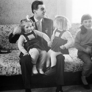 Man sits with three young girls on a floral sofa.