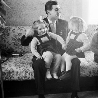 Man sits with three young girls on a floral sofa.