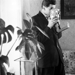 Man in suit uses vintage film camera indoors.