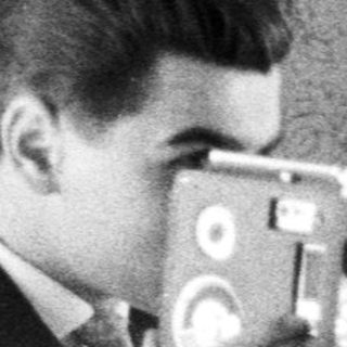 Man in suit uses vintage film camera indoors.
