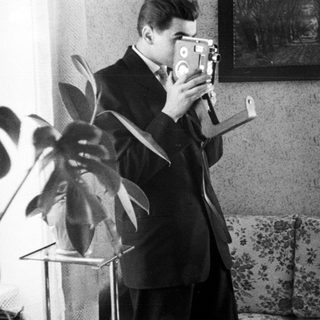 Man in suit uses vintage film camera indoors.