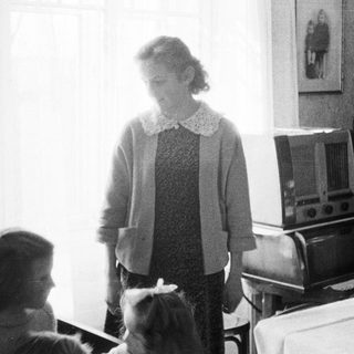 Woman standing near a radio in a vintage room.