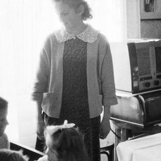 Woman standing near a radio in a vintage room.