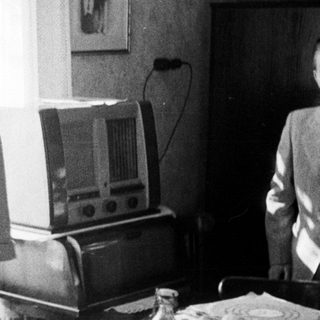 Woman standing near a radio in a vintage room.