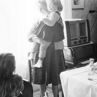 Woman holds child near table with vintage radio.