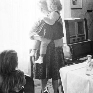 Woman holds child near table with vintage radio.