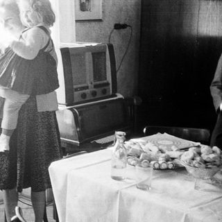 Woman holds child near table with vintage radio.