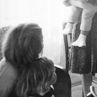 Woman holds child near table with vintage radio.