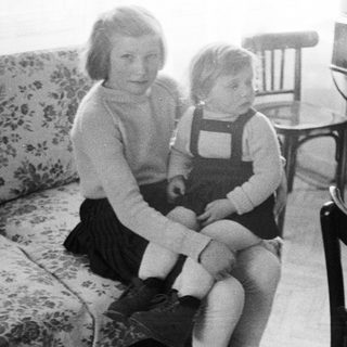 Girl sits with a child on a floral couch.