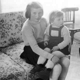 Girl sits with a child on a floral couch.