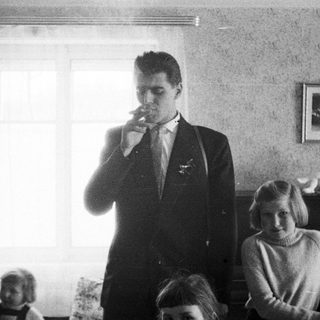 Man smoking in a room, two girls nearby.