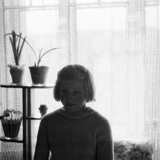 Young girl stands near plants and a window.