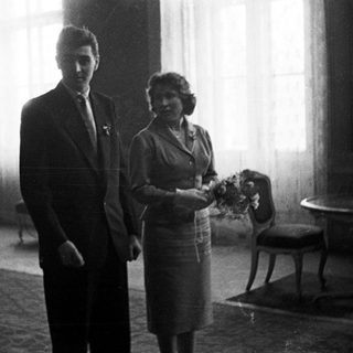 Couple stands in room, likely after a wedding.