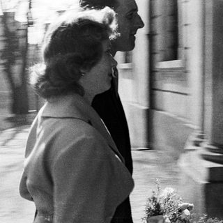 Couple walks outdoors, likely during a wedding or formal event.