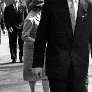 Two men in suits walking outdoors, with others in background.