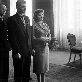 Three people stand in a room, formally dressed.