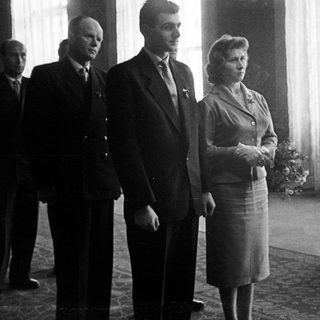 Three people stand in a room, formally dressed.