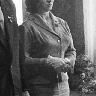 Three people stand in a room, formally dressed.