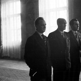Three men in suits stand in a dimly lit room.