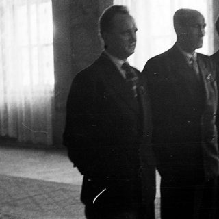 Three men in suits stand in a dimly lit room.