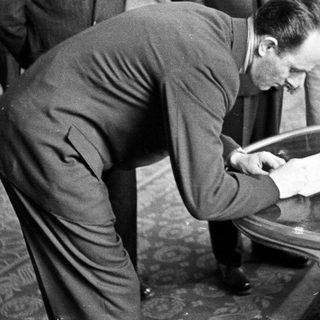 Man in suit writes on a table indoors.