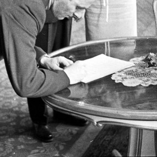 Man in suit writes on a table indoors.